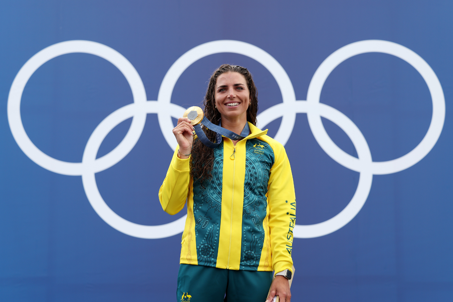 Jessica Fox holding a gold medal in front of the olympic rings. 