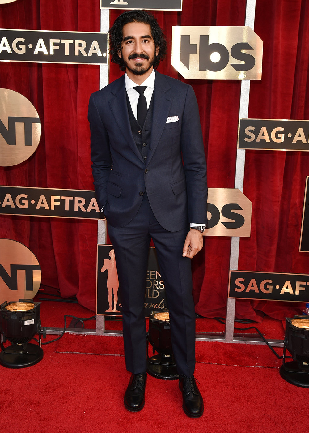 Man in a navy suit on the red carpet at the SAG-AFTRA event, standing in front of a red velvet backdrop.