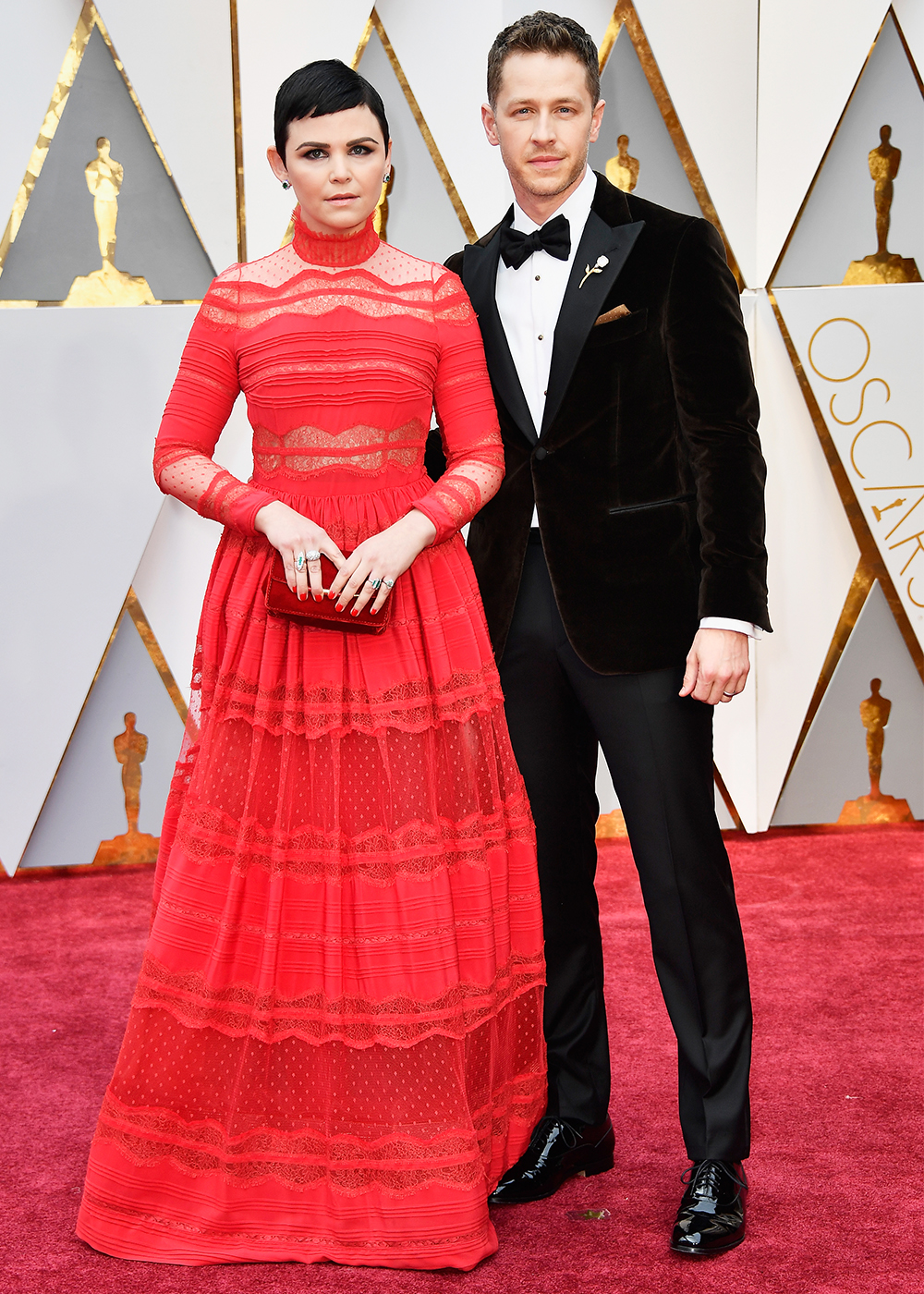 Woman in red gown and man in tuxedo pose together on a red carpet event.